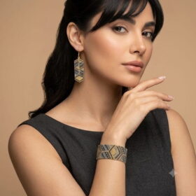 Model wearing handmade gold-toned and grey geometric beaded cuff bracelet and matching drop earrings.