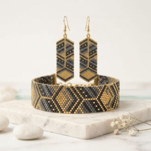 Close-up product display of gold-toned and grey beaded drop earrings and matching cuff on white marble.
