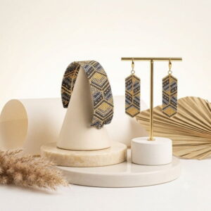 Minimalist studio scene showing gold-toned grey beaded jewelry set on white podiums with palm accents.
