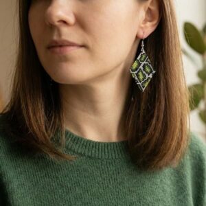 Front portrait of a woman wearing sophisticated green, black, and gold-toned woven seed bead earrings.
