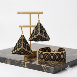 Black and gold-toned beaded pyramid earrings and cuff bracelet on a display stand.