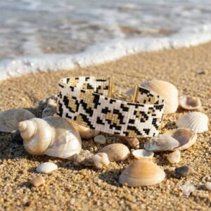 Handmade leopard print beaded cuff bracelet styled on a sandy beach surrounded by natural seashells.
