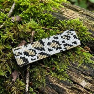 Flat lay view of the handmade black and metallic gold-finish seed bead bracelet resting on green forest moss.