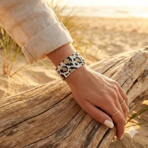 Close-up of a woman's wrist showcasing the handmade beaded statement bracelet while resting on a sun-bleached beach log.