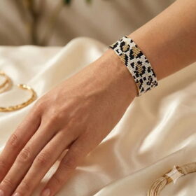 Side profile view of the luxurious gold-and-black palette beaded cuff bracelet worn on a model's wrist over satin sheets.