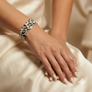 A sophisticated shot of a woman with neutral manicured nails gently folding her hands to display the artisan beaded cuff jewelry.