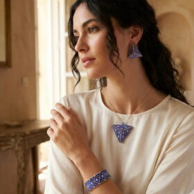 Lifestyle shot of a woman wearing the artisanal royal blue woven bead jewelry set with a classic silk blouse.