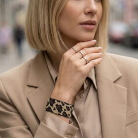 A close-up of a woman in a sophisticated beige blazer showcasing the Leopard Loom Beaded Cuff on her wrist.