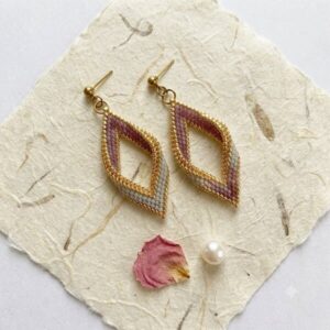 Pair of hand-woven mauve and gold-toned diamond earrings on handmade paper with a pearl and rose petal.