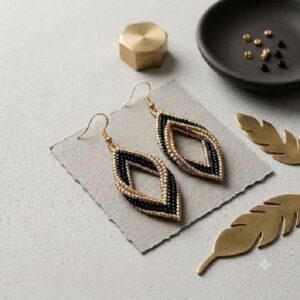 Flat lay of black and gold-finish beaded diamond earrings on grey paper with brass decorative feathers.