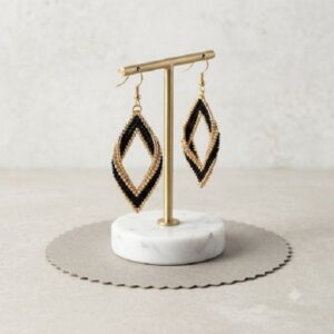 Gold-toned and black 3D beaded drop earrings displayed on a gold T-bar on a marble base.