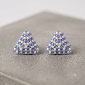 Pair of 3D periwinkle and cream beaded triangle stud earrings on concrete background.