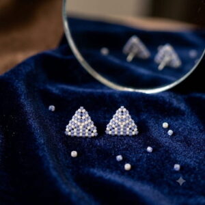 Periwinkle triangle beaded studs displayed on rich dark blue velvet with mirror reflection.