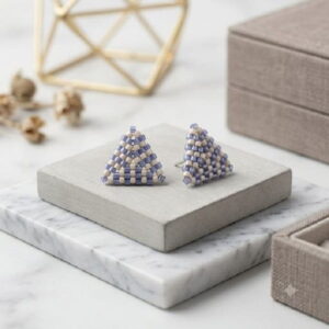 Beaded periwinkle triangle stud earrings set on concrete and white marble tiles.