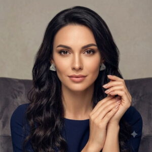 Portrait of a woman with dark hair wearing silver beaded triangle statement earrings.