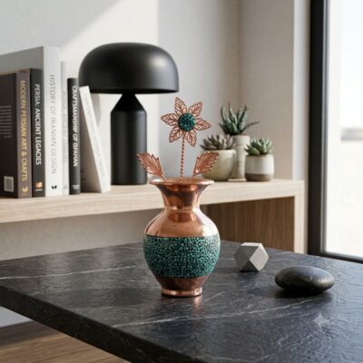 Handcrafted mini copper flower vase with turquoise inlay on a black marble table next to art books.